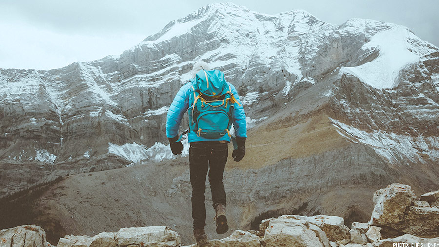 man in blue jacket and black pants hiking on rock mountain during daytime